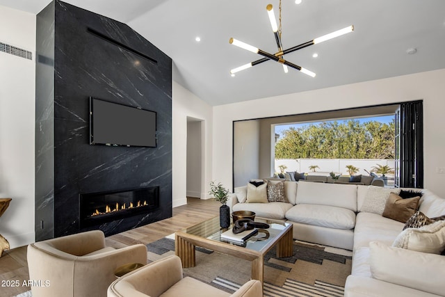 living room with vaulted ceiling, a notable chandelier, a fireplace, and light hardwood / wood-style floors