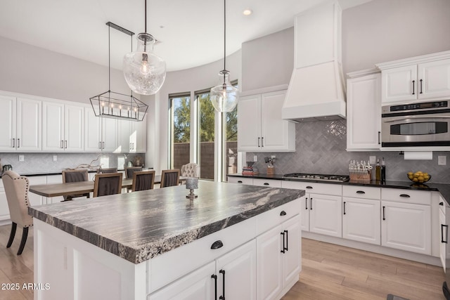 kitchen featuring hanging light fixtures, stainless steel appliances, a center island, custom range hood, and white cabinets