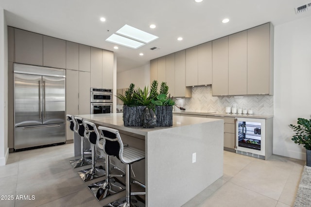 kitchen with a center island, appliances with stainless steel finishes, gray cabinets, beverage cooler, and backsplash