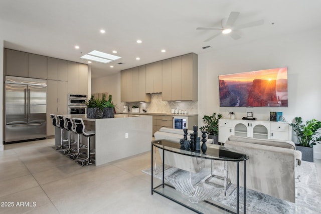 kitchen with stainless steel appliances, a large island, gray cabinetry, and a kitchen bar