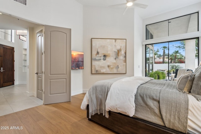 bedroom with ceiling fan, a towering ceiling, access to exterior, and light hardwood / wood-style floors