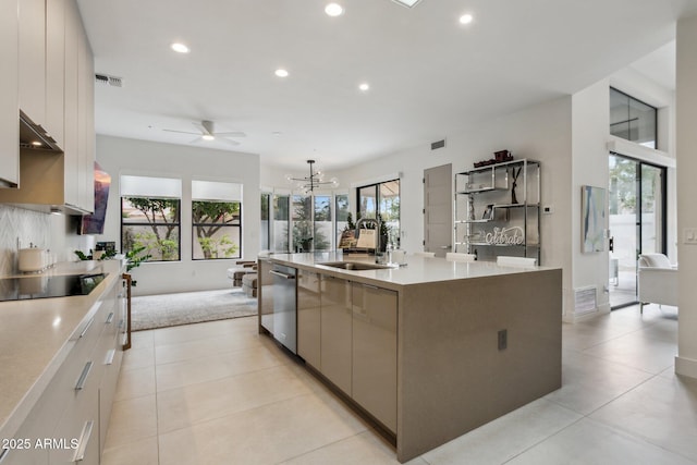 kitchen with sink, light tile patterned flooring, black electric cooktop, stainless steel dishwasher, and a large island with sink