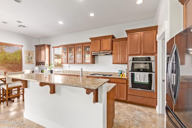 kitchen with light stone countertops, light tile patterned floors, a breakfast bar area, stainless steel appliances, and a center island with sink