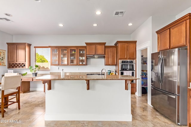 kitchen with a kitchen breakfast bar, an island with sink, light stone countertops, light tile patterned floors, and stainless steel appliances