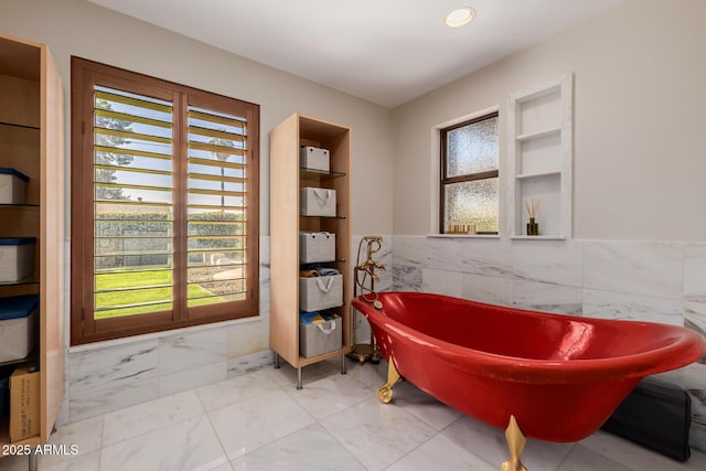 full bathroom featuring a healthy amount of sunlight, a freestanding tub, marble finish floor, and tile walls