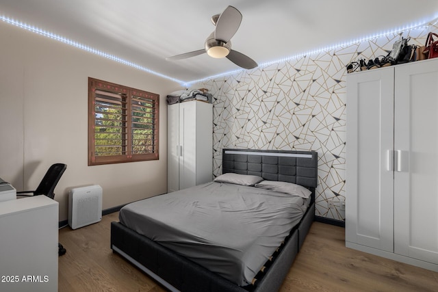 bedroom featuring wallpapered walls, baseboards, ceiling fan, an accent wall, and wood finished floors