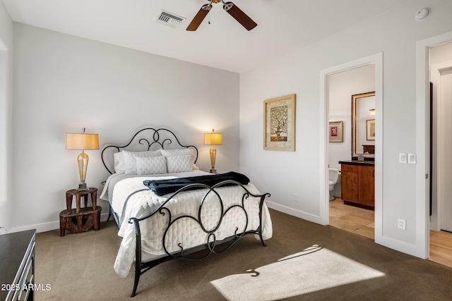 carpeted bedroom featuring ceiling fan, visible vents, baseboards, and ensuite bath