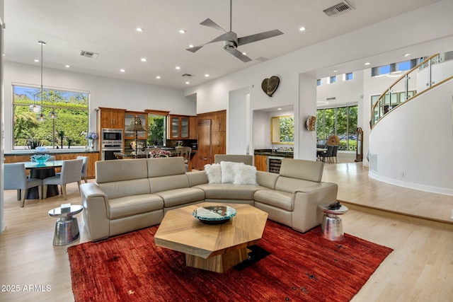 living area featuring visible vents, stairs, light wood-style floors, and a towering ceiling