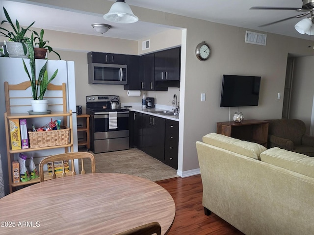 8221 E Garfield St Unit L109, Scottsdale, AZ 85257 - kitchen featuring stainless steel appliances, dark cabinetry, light wood-style flooring, a ceiling fan, and light countertops