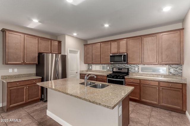 kitchen featuring appliances with stainless steel finishes, sink, backsplash, light stone counters, and a center island with sink