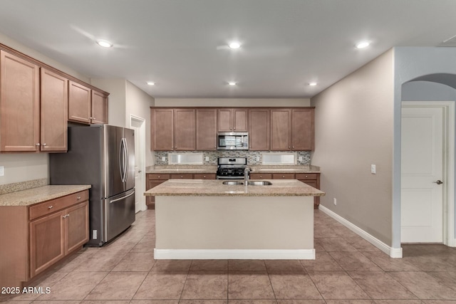 kitchen with light tile patterned floors, an island with sink, stainless steel appliances, tasteful backsplash, and sink