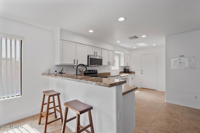 4323 E Dublin St, Gilbert, AZ 85295 - kitchen with stainless steel microwave, a kitchen bar, black range with electric stovetop, a peninsula, and white cabinets