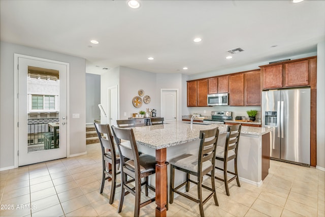 kitchen with stainless steel appliances, light stone countertops, a center island with sink, and a kitchen breakfast bar