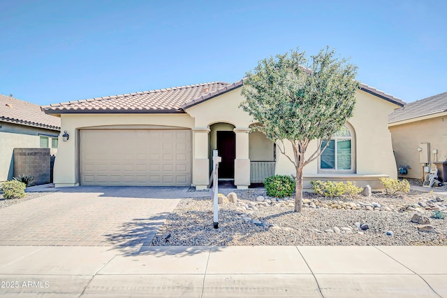 mediterranean / spanish-style house with decorative driveway, a tile roof, an attached garage, and stucco siding