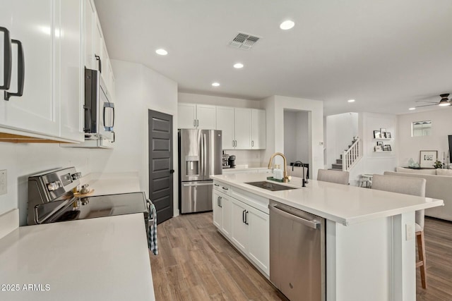 kitchen with a center island with sink, sink, appliances with stainless steel finishes, light hardwood / wood-style floors, and white cabinetry