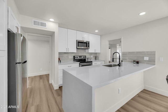 kitchen with stainless steel appliances, a sink, a peninsula, light wood-style floors, and recessed lighting