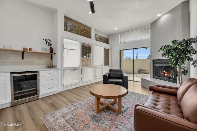 living area with beverage cooler, a large fireplace, light wood finished floors, and recessed lighting