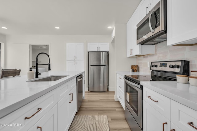 kitchen with stainless steel appliances, a sink, light countertops, tasteful backsplash, and white cabinetry