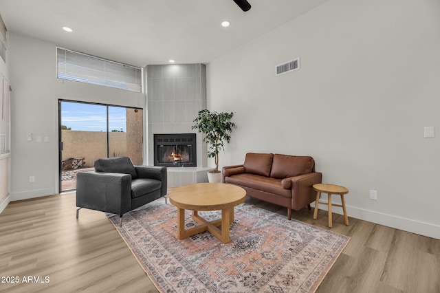 living area with a tiled fireplace, baseboards, light wood-type flooring, recessed lighting, and a ceiling fan