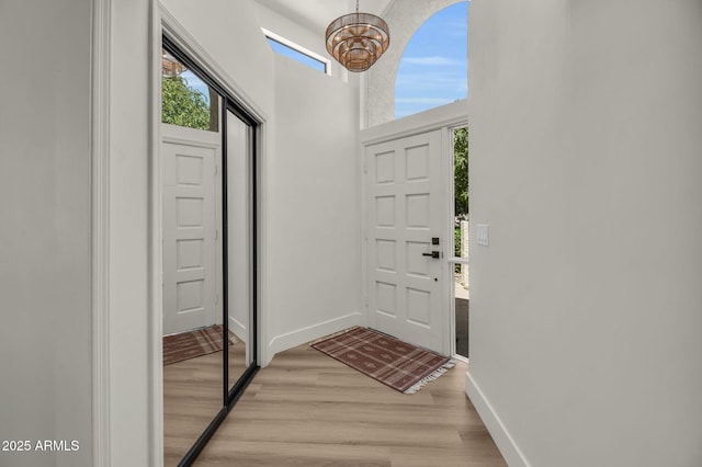 entryway with a chandelier, light wood-type flooring, baseboards, and a towering ceiling