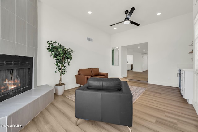 living room featuring light wood-style flooring, ceiling fan, a tiled fireplace, recessed lighting, and baseboards