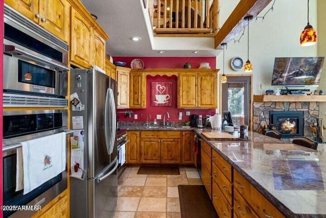 kitchen featuring pendant lighting, sink, stainless steel appliances, dark stone countertops, and a stone fireplace