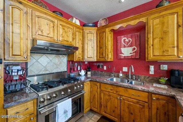 kitchen featuring sink, dark stone counters, stainless steel stove, and a textured ceiling