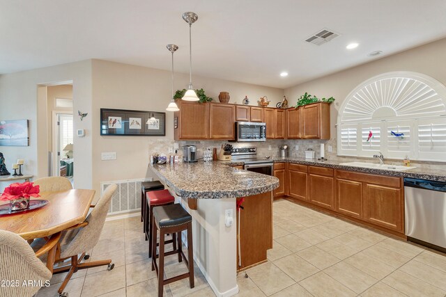 4245 E Ficus Way, Gilbert, AZ 85298 - kitchen featuring appliances with stainless steel finishes, a sink, a peninsula, brown cabinets, and a breakfast bar