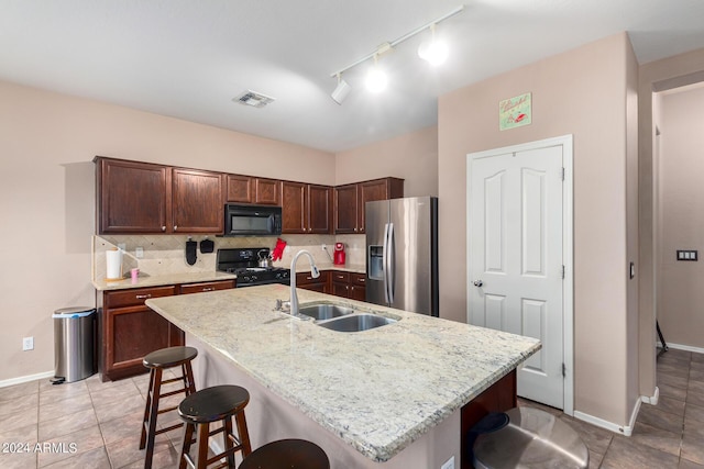 kitchen with an island with sink, sink, a kitchen breakfast bar, decorative backsplash, and black appliances