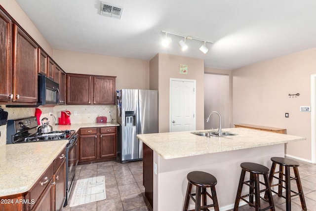 kitchen with gas range, stainless steel fridge, and a center island with sink