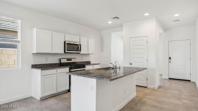 kitchen featuring white cabinetry, sink, gas range oven, dark stone counters, and a center island with sink