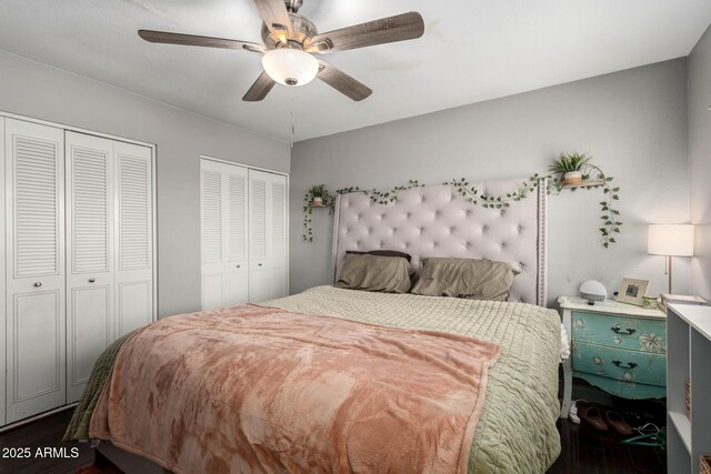 bedroom featuring dark wood-style floors, a ceiling fan, and two closets