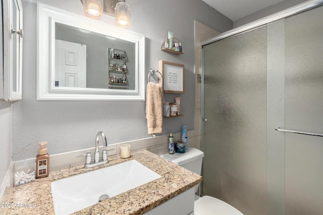 full bath featuring toilet, vanity, a textured wall, and a shower stall