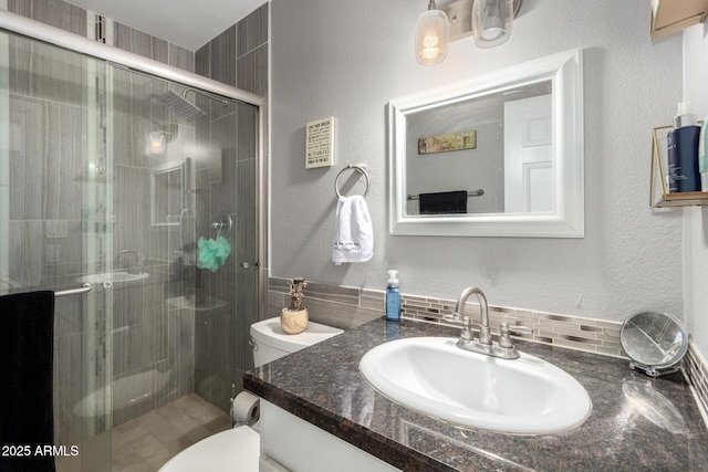 bathroom featuring vanity, a textured wall, toilet, and a shower stall