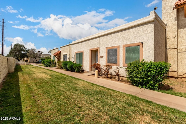 rear view of house featuring a lawn and stucco siding