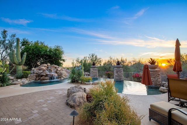 pool at dusk featuring pool water feature and a patio