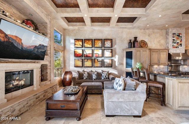 living room featuring beam ceiling, a stone fireplace, and coffered ceiling