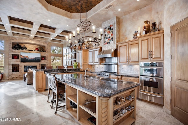 kitchen featuring a center island with sink, decorative light fixtures, a towering ceiling, and stainless steel appliances