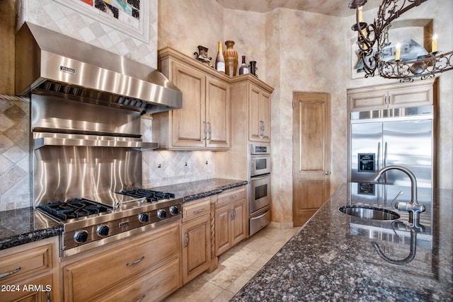 kitchen featuring appliances with stainless steel finishes, tasteful backsplash, dark stone counters, sink, and hanging light fixtures