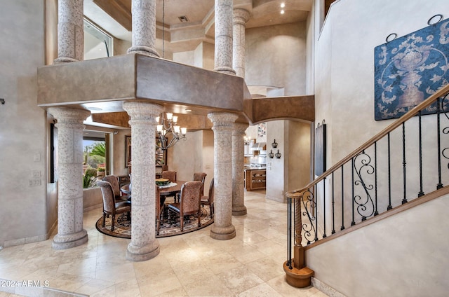 interior space featuring a towering ceiling, an inviting chandelier, and ornate columns