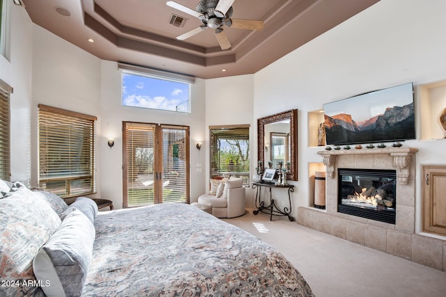 bedroom with french doors, a towering ceiling, ceiling fan, a fireplace, and carpet floors