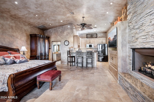 bedroom with a stone fireplace, black fridge, and a towering ceiling