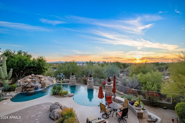 pool at dusk featuring pool water feature and a patio area