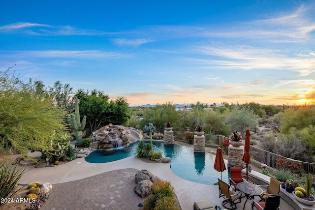 pool at dusk with a patio area and pool water feature