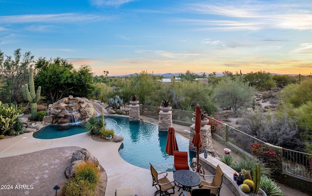 pool at dusk with pool water feature and a patio