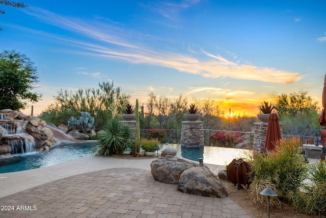 pool at dusk with pool water feature and a patio