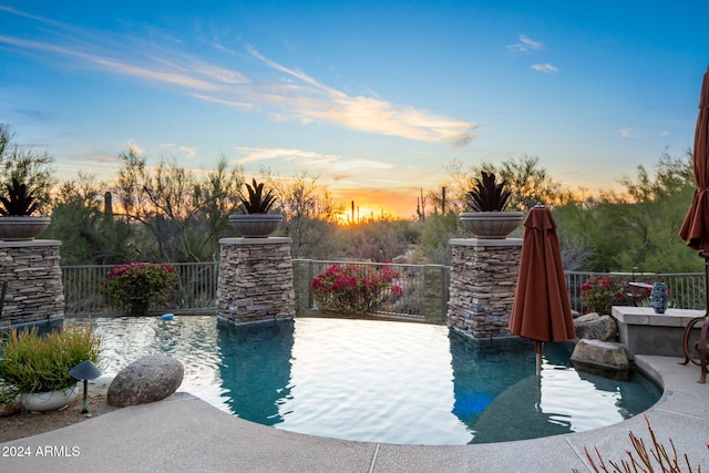 pool at dusk with a patio area and an outdoor stone fireplace