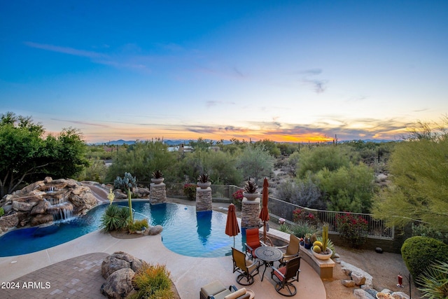 pool at dusk featuring pool water feature and a patio