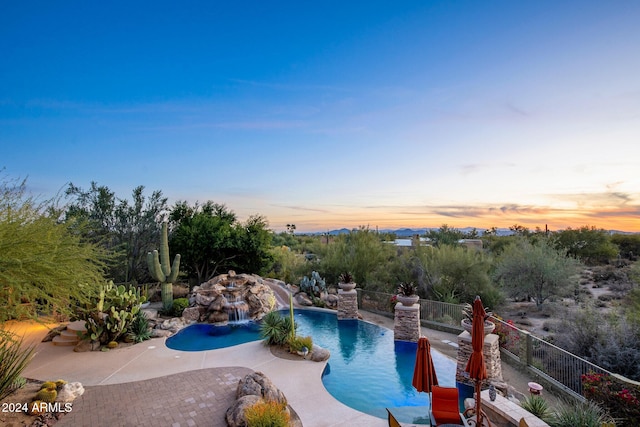 pool at dusk featuring pool water feature and a patio