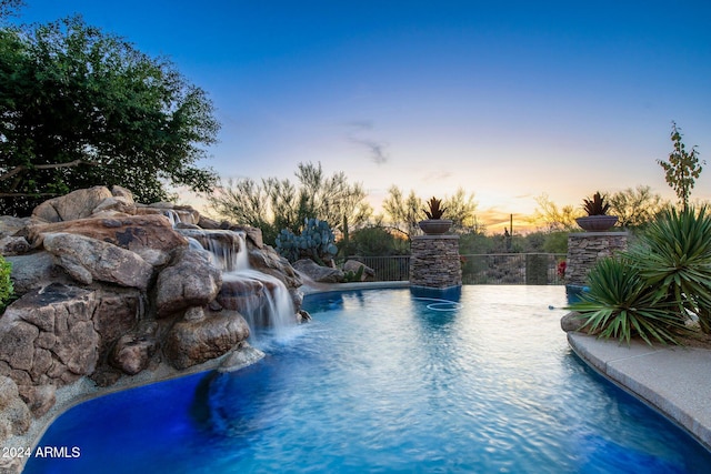 pool at dusk featuring pool water feature